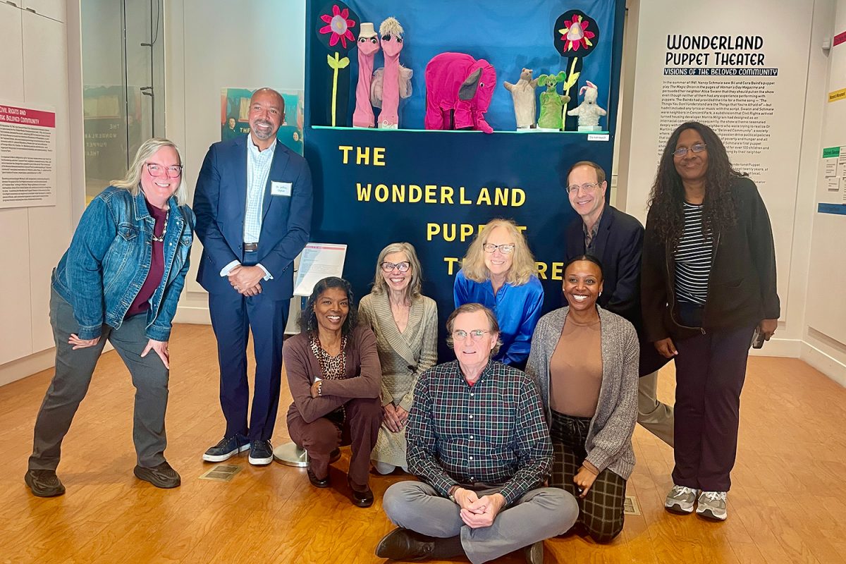 A group of participants poses in front of a display of puppets at the Wonderland Puppet Theater Symposium. 