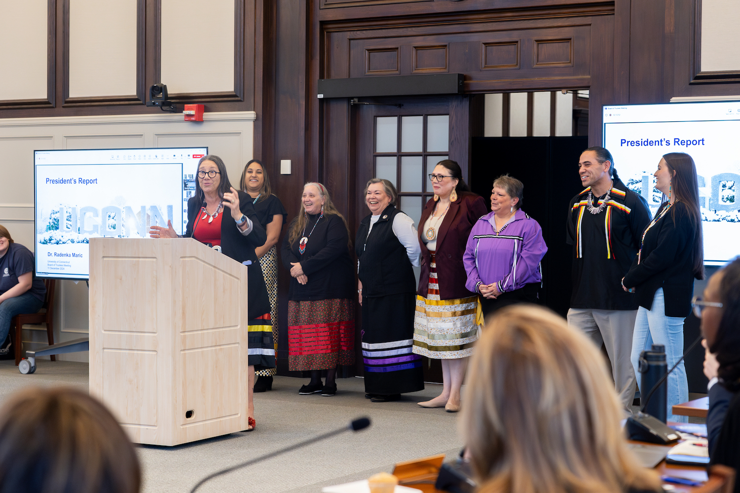 Beth Regan speaks at a podium backed by members of other tribal nations.